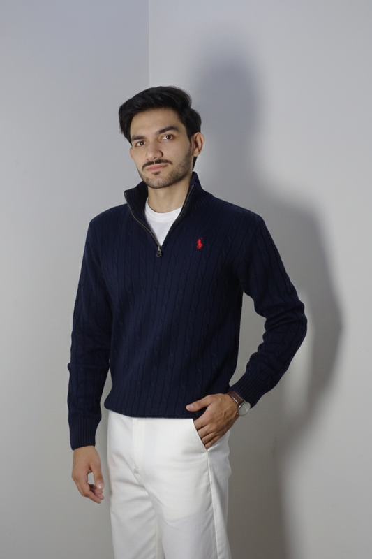 Man wearing a navy sweater with a red logo and white pants against a plain background