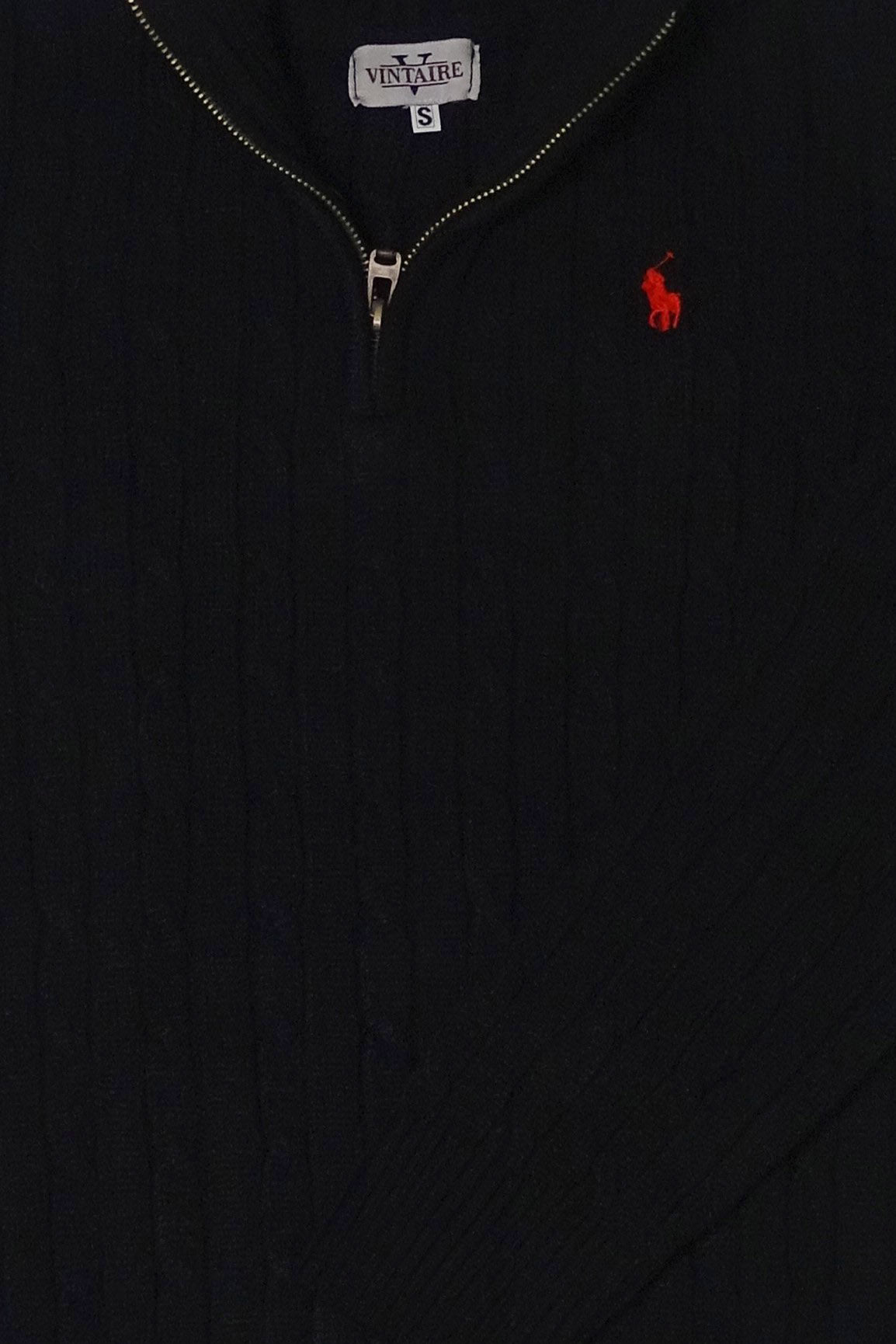 Close-up of a black sweater with a red embroidered logo on a dark background