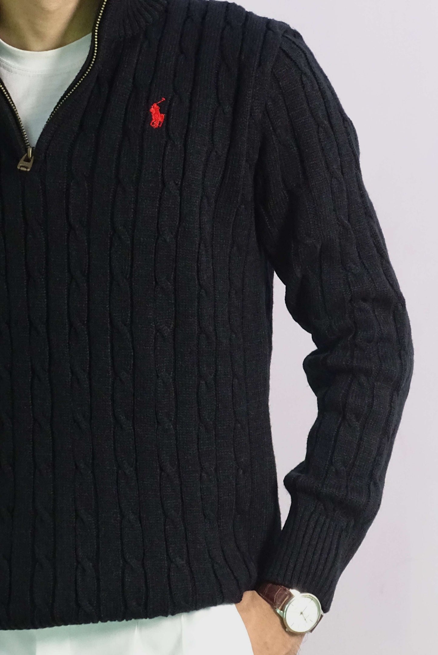 Black cable knit sweater with a red logo on a light gray background
