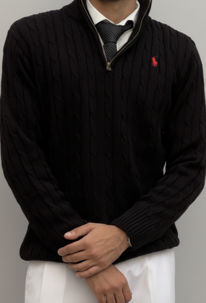 Person wearing a black cable knit sweater with a red logo on a gray background