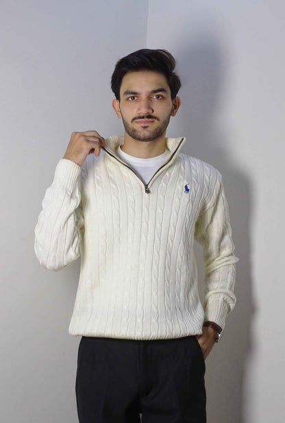 Man wearing a white cable knit sweater with a brand logo against a plain background