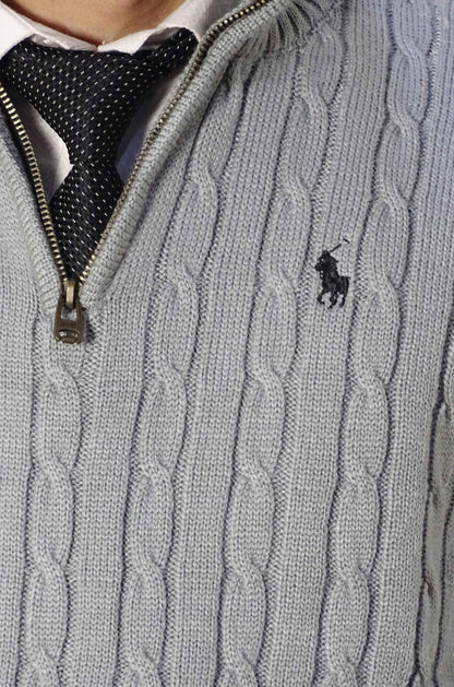 Gray cable knit sweater with a brand logo on a person wearing a white shirt and black tie.