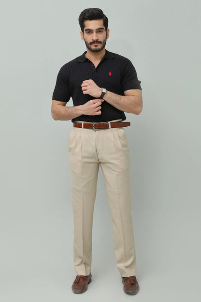 Man wearing a black polo shirt with a logo, beige pants, and brown shoes on a gray background