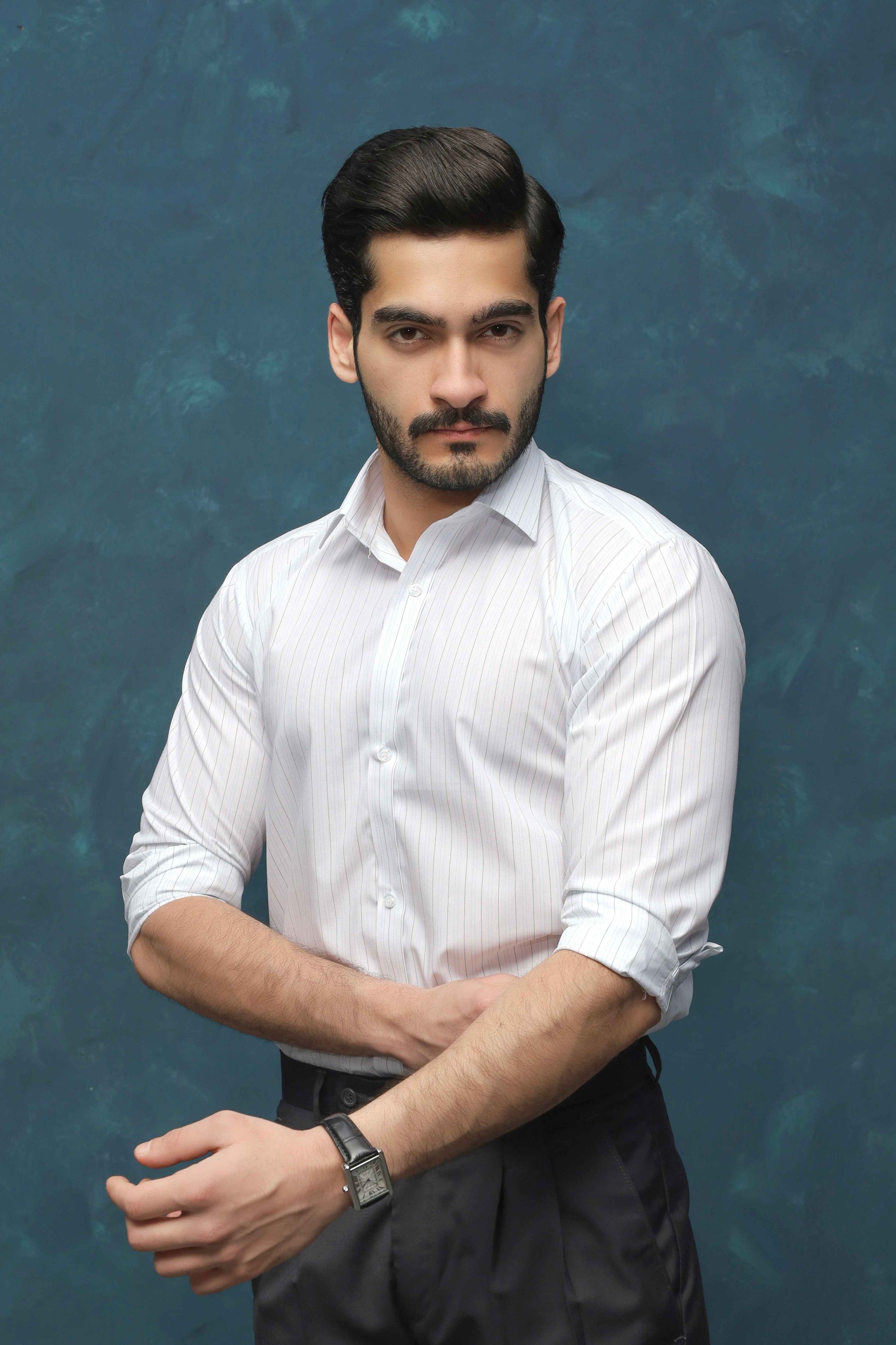 Man wearing a white shirt and dark pants against a textured blue background