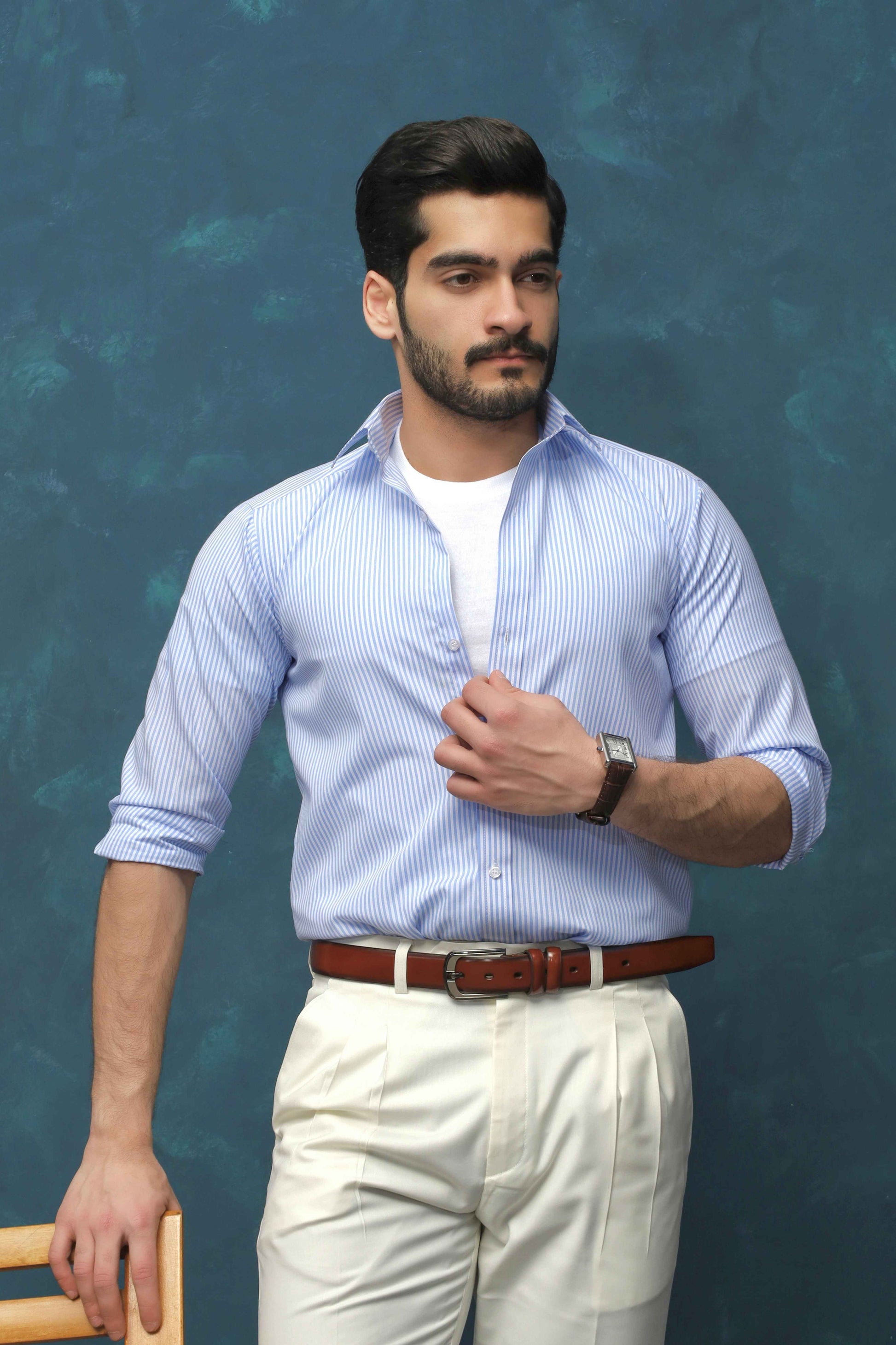 Man wearing a light blue shirt and white pants against a textured blue background
