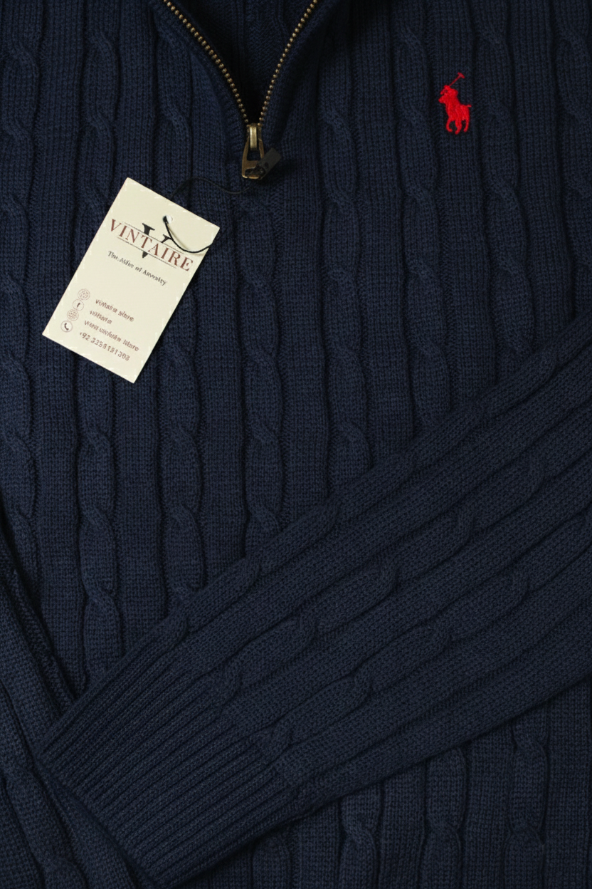 Navy cable knit sweater with a red logo tag on a dark background