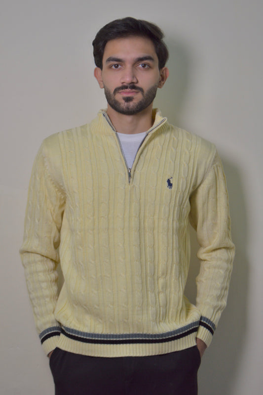 Man wearing a light yellow cable knit sweater with a brand logo against a plain background