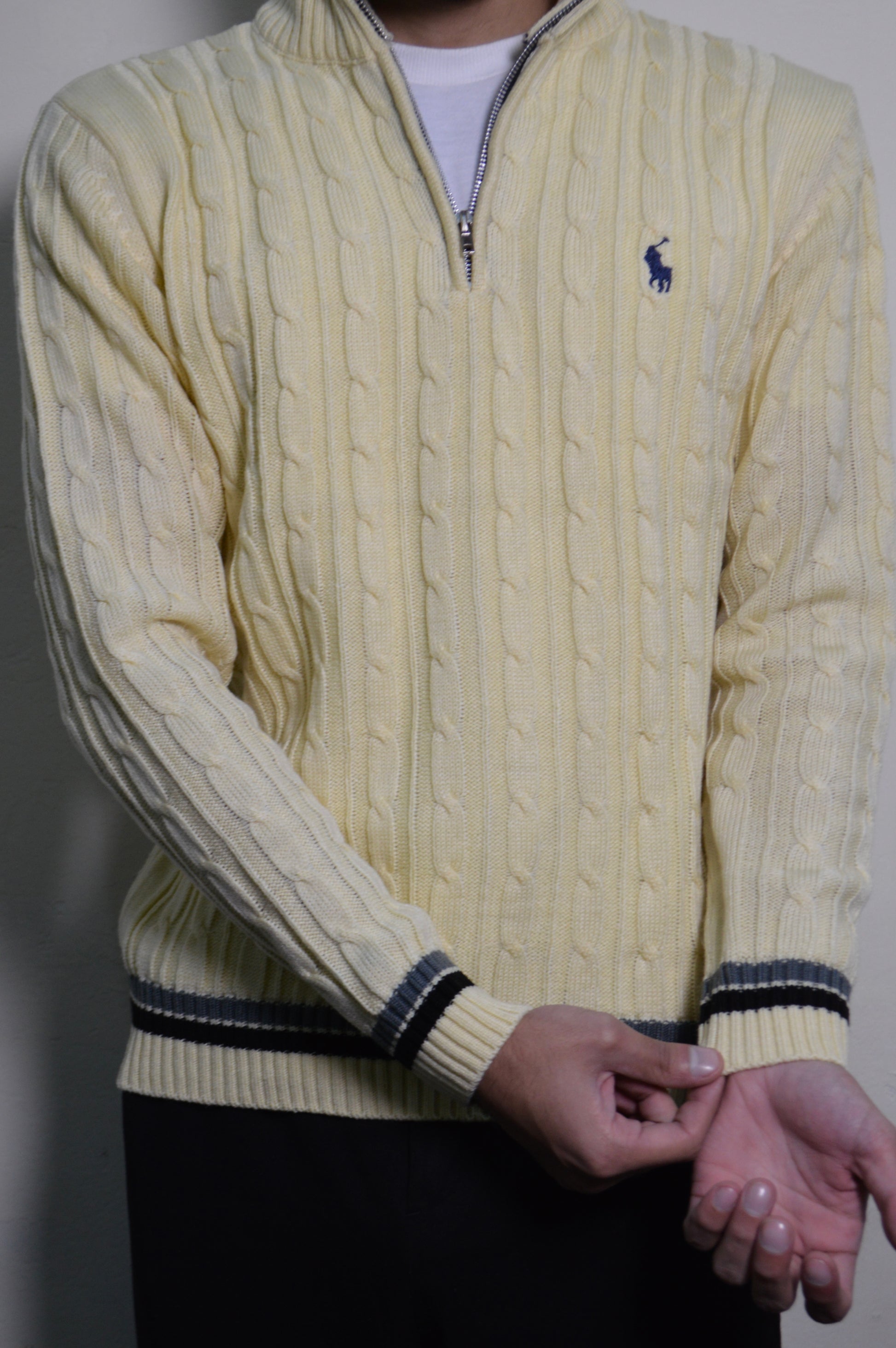 Yellow cable knit sweater with a brand logo on a plain background